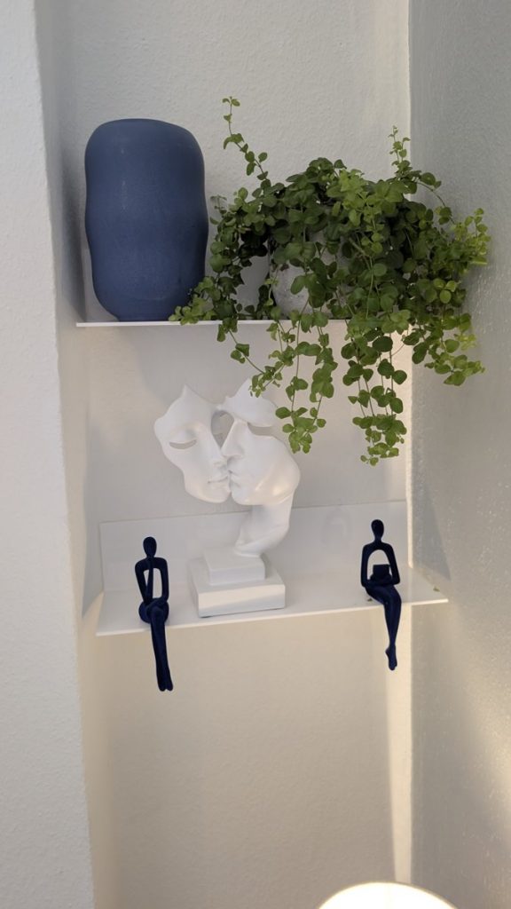 Wandregal in der Praxis: weiße Skulptur zweier einander zugewandter Gesichter, blaue Figuren und Grünpflanze