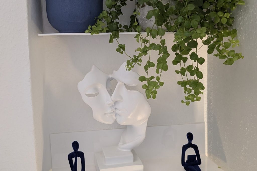 Weiße Skulptur zweier einander zugewandter Gesichter auf einem Wandregal in der Praxis