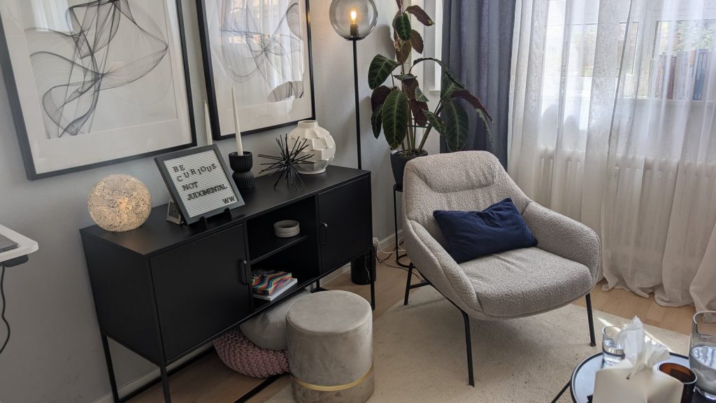Sessel und schwarzes Sideboard mit dem Letterboard „Be curious, not judgmental" im Therapieraum der Praxis