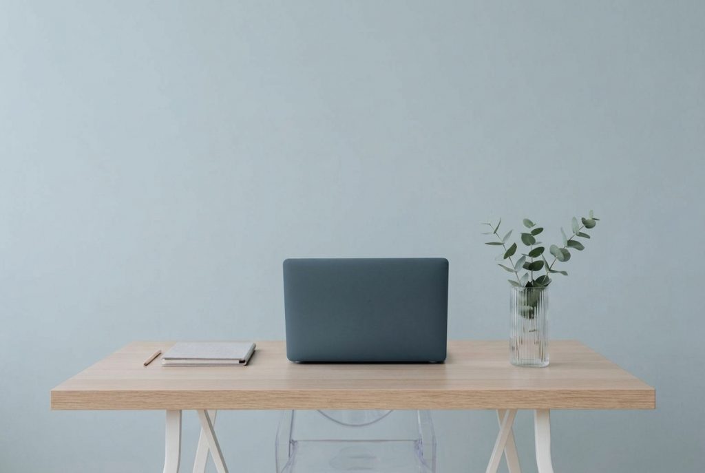 Laptop auf aufgeraeumtem Schreibtisch vor hellblauer Wand